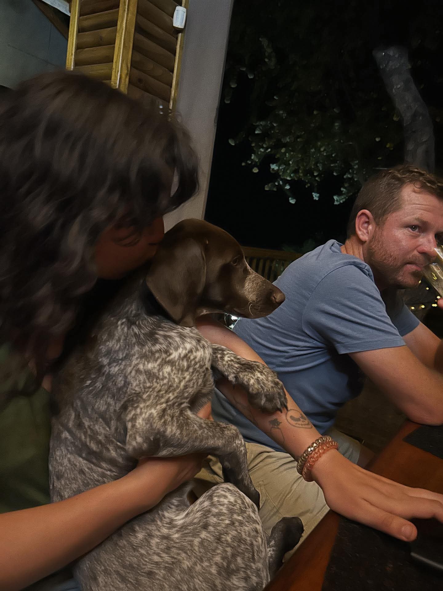 Angelo and friends cuddling a German shorthaired pointer at a table at night