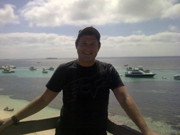Angelo at a railing overlooking a yacht-filled bay below