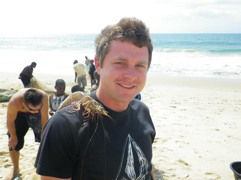Angelo smiling on the beach with a crayfish resting on his shoulder while others pull nets behind