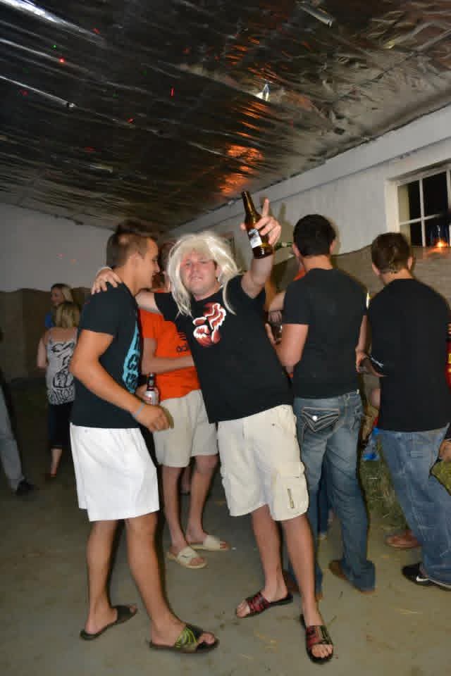 Angelo in a white wig raising a beer while dancing with friends