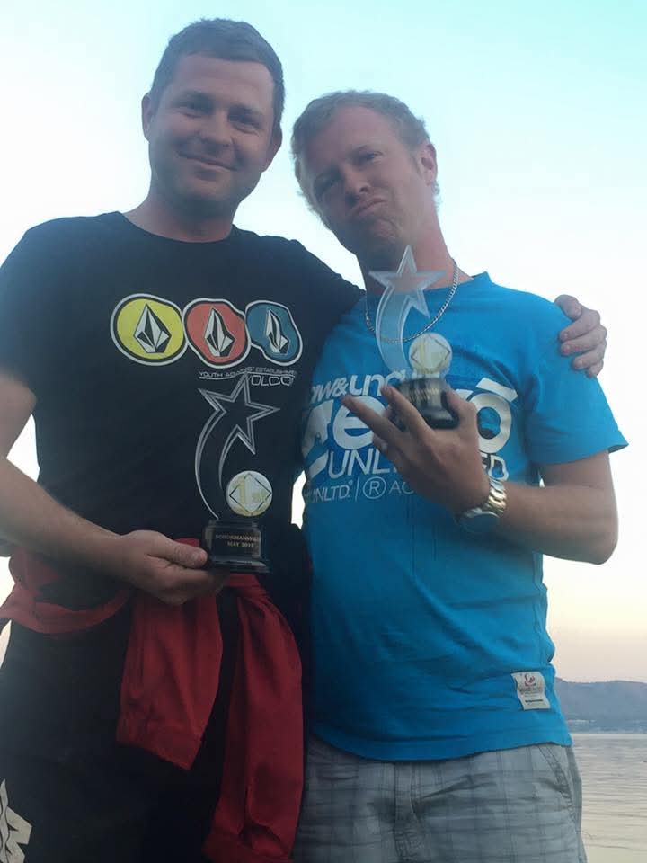Angelo and a friend holding trophies together at dusk beside the water