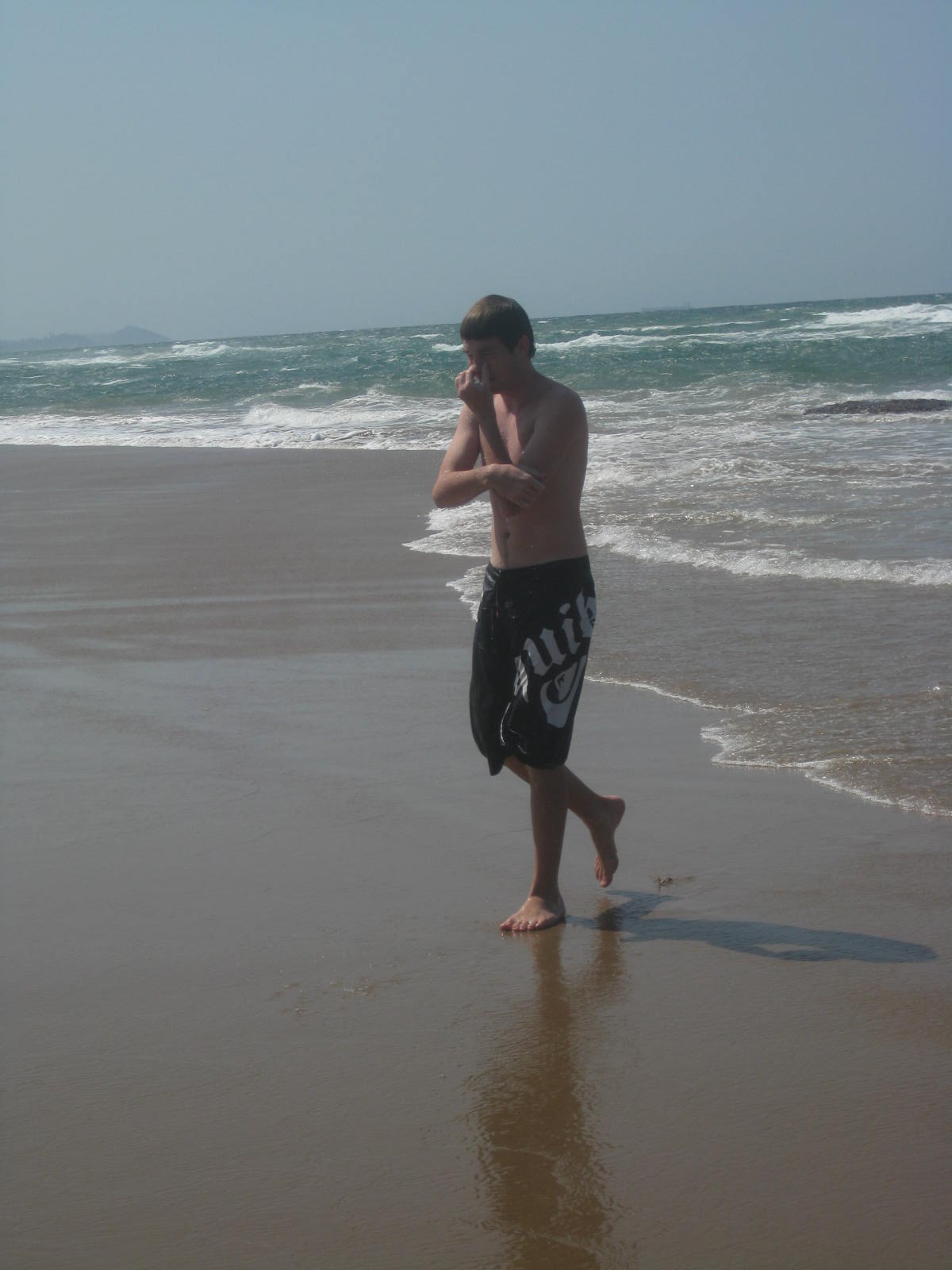 Angelo walking barefoot along the beach beside breaking waves