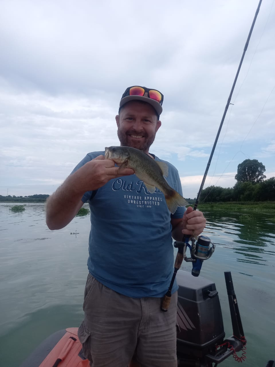 Angelo proudly holding a bass with his rod in the other hand on the river