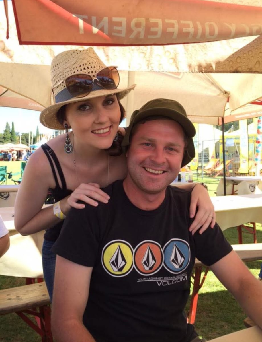 A friend leaning over Angelo's shoulder as he sits at a festival table