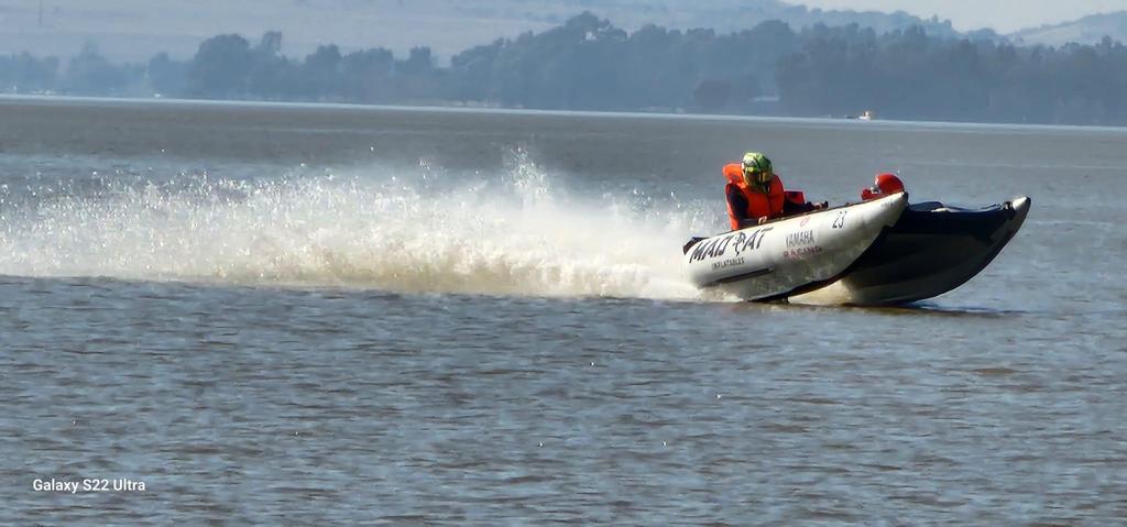 A white inflatable racing boat banking across the lake with a long trail of spray