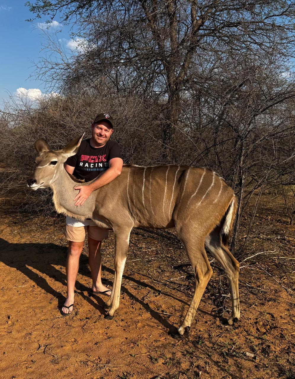 Angelo hugging a young kudu on red bushveld earth