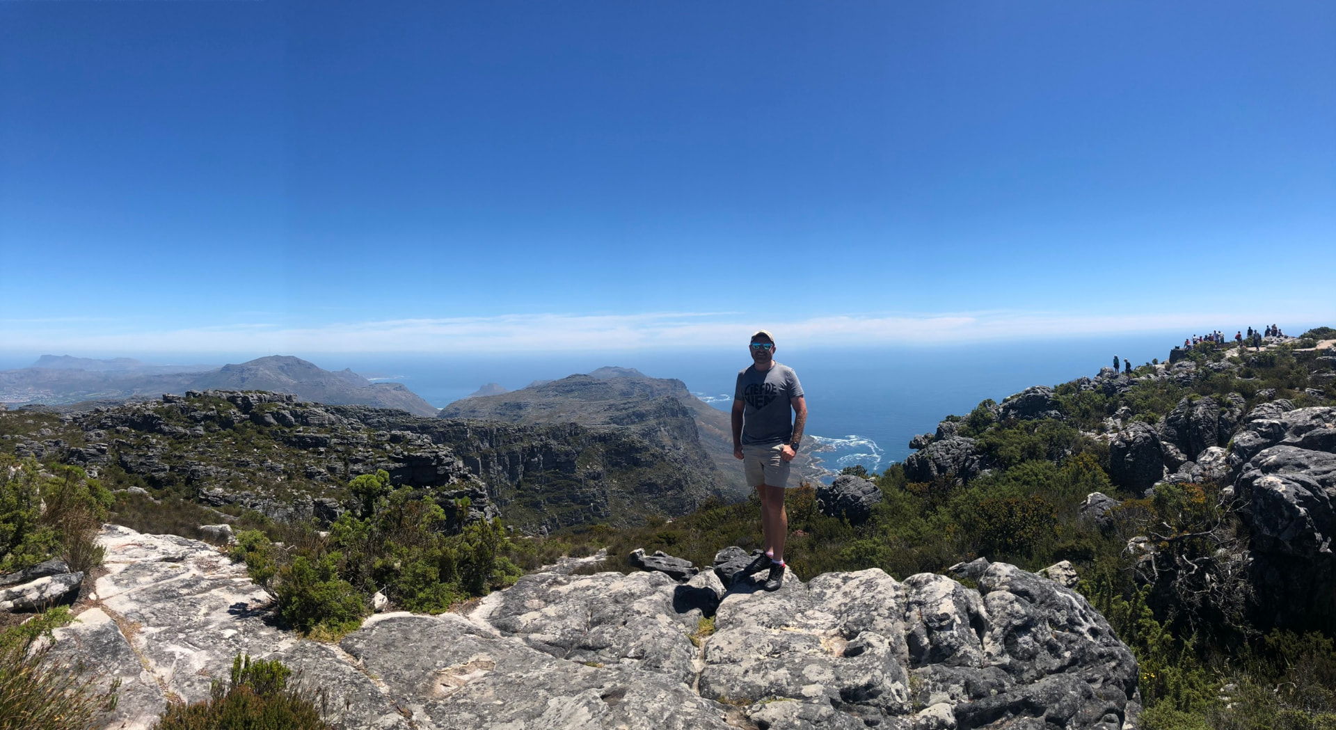 Angelo standing on rocks with a broad mountain and ocean panorama behind him