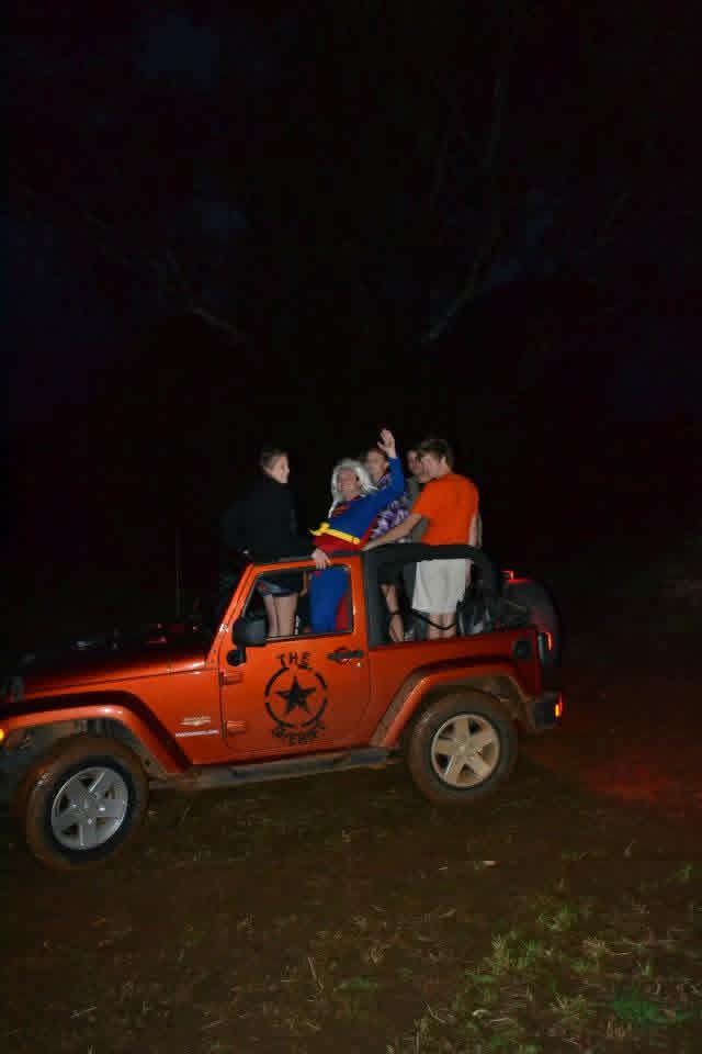 Friends gathered on the back of an orange jeep in the dark during the party