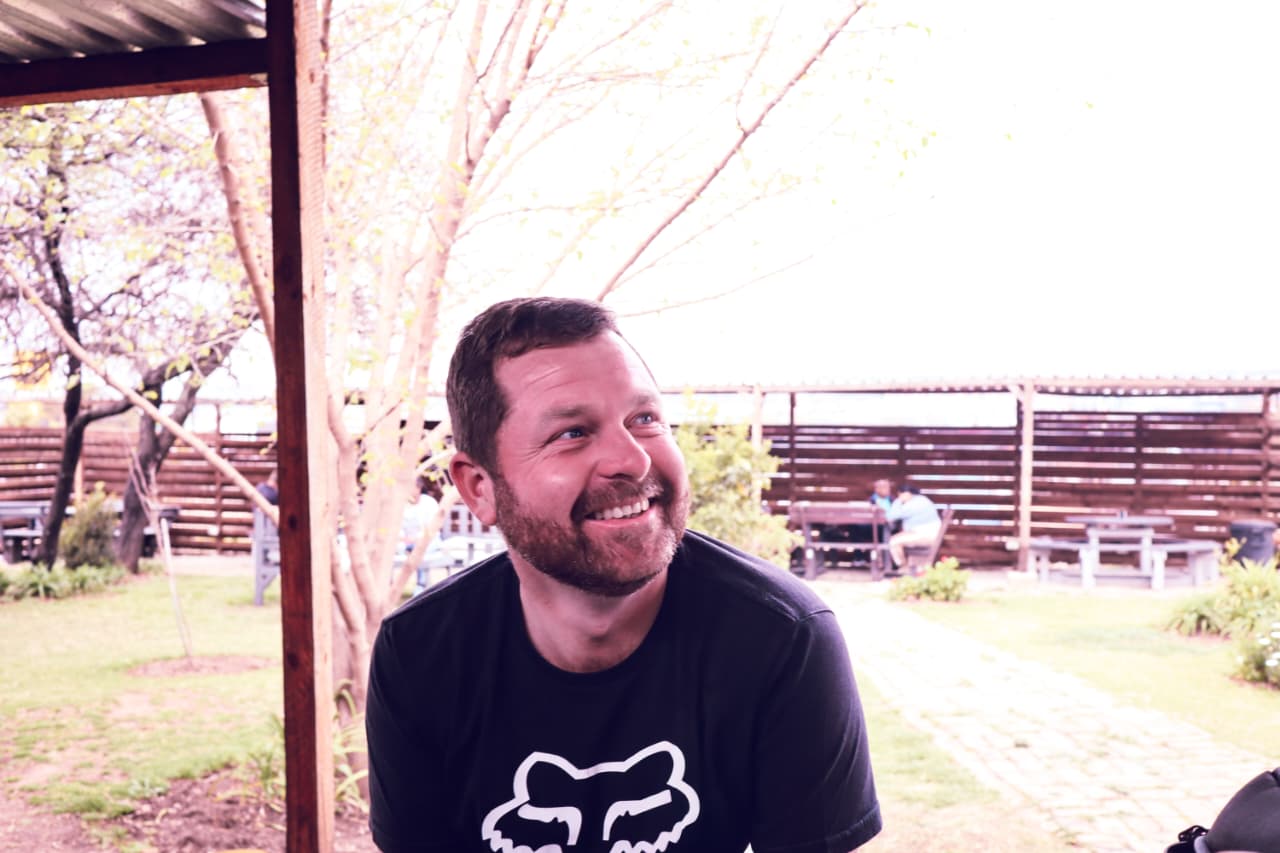 Angelo smiling in a black Fox Racing shirt beneath a garden patio roof