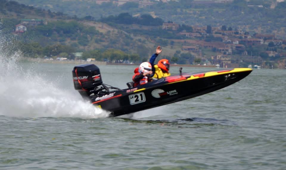 Angelo waving from a speeding racing boat on a lake