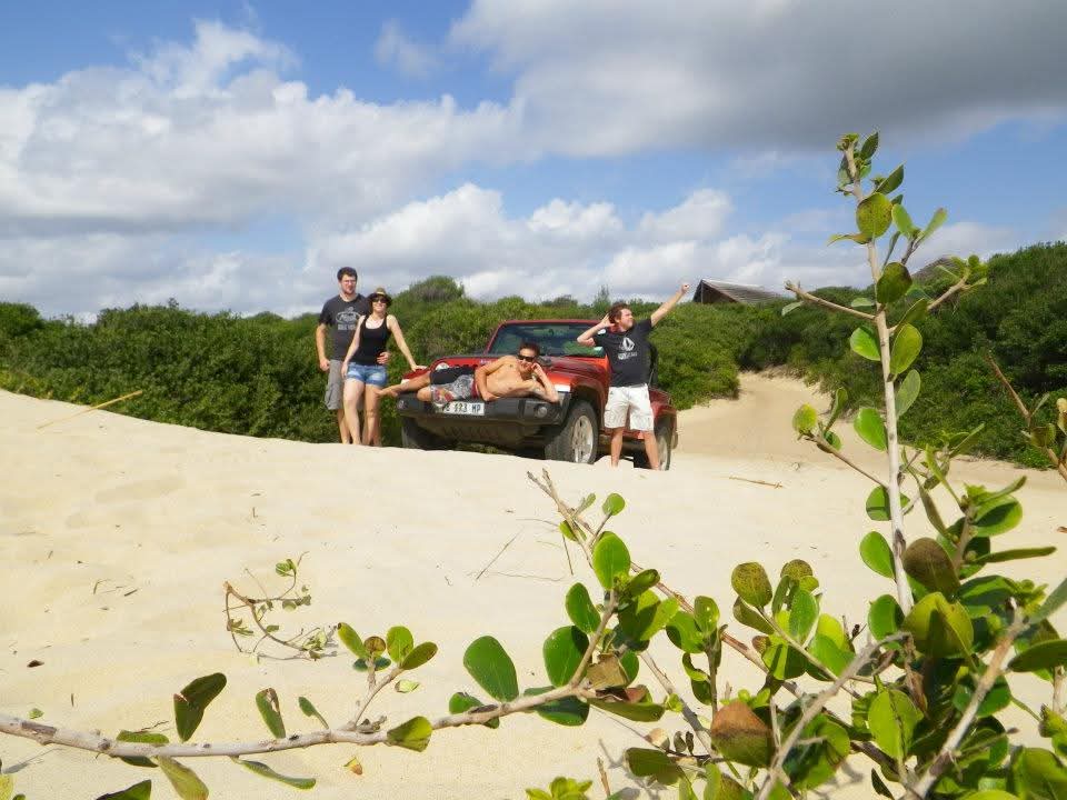 Four friends around a red jeep parked on top of a sand dune