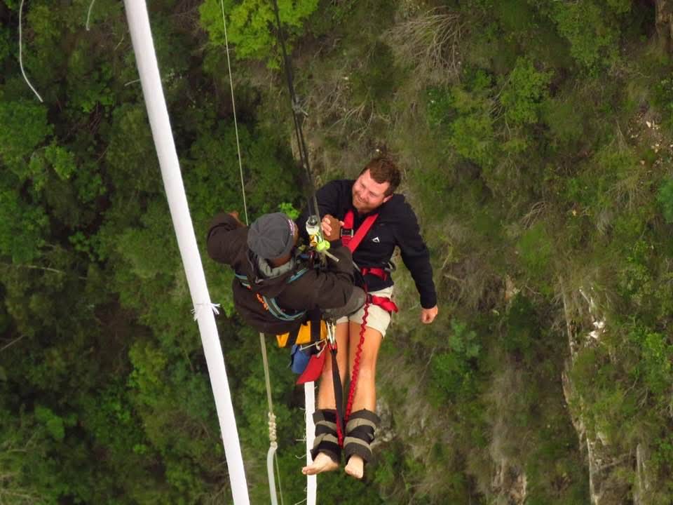 Angelo seated on the bungy platform beam smiling as the guide reaches him after the jump
