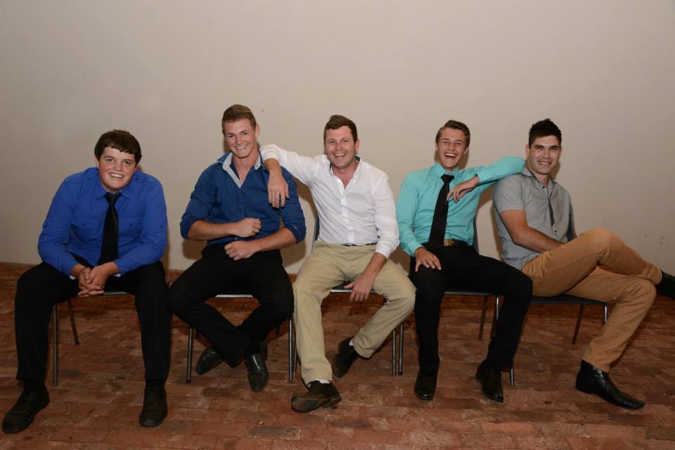 Five young men sitting in a row smiling for a portrait