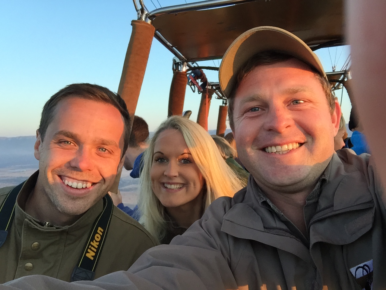 Three friends taking a selfie in a hot-air balloon high above the landscape at dawn