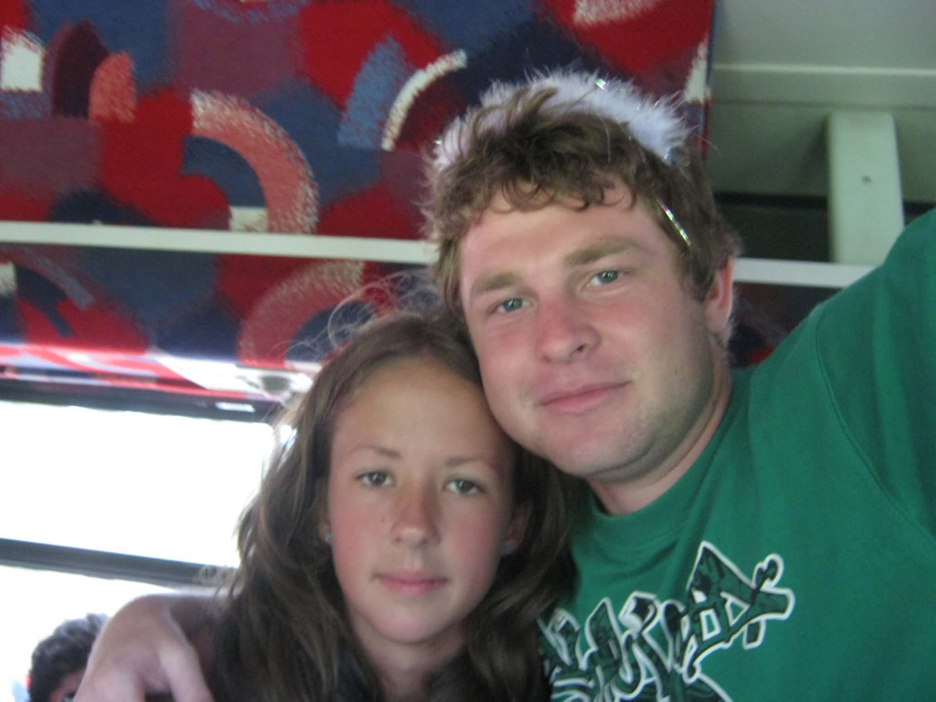 Angelo in a green shirt with a feather halo beside a young girl on a bus