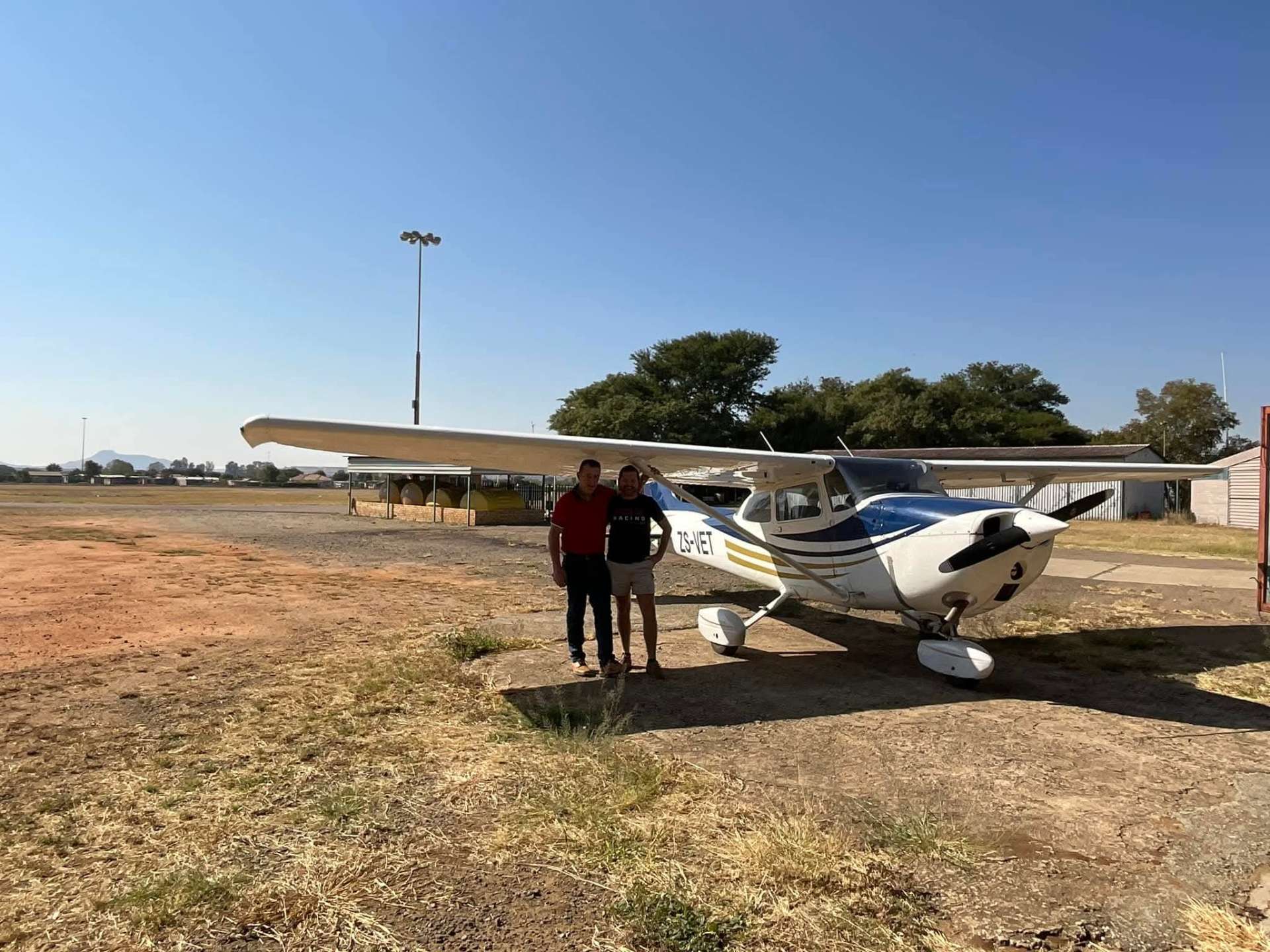 Angelo and a man in a red shirt standing together beside Cessna ZS-VET on a sunny airfield