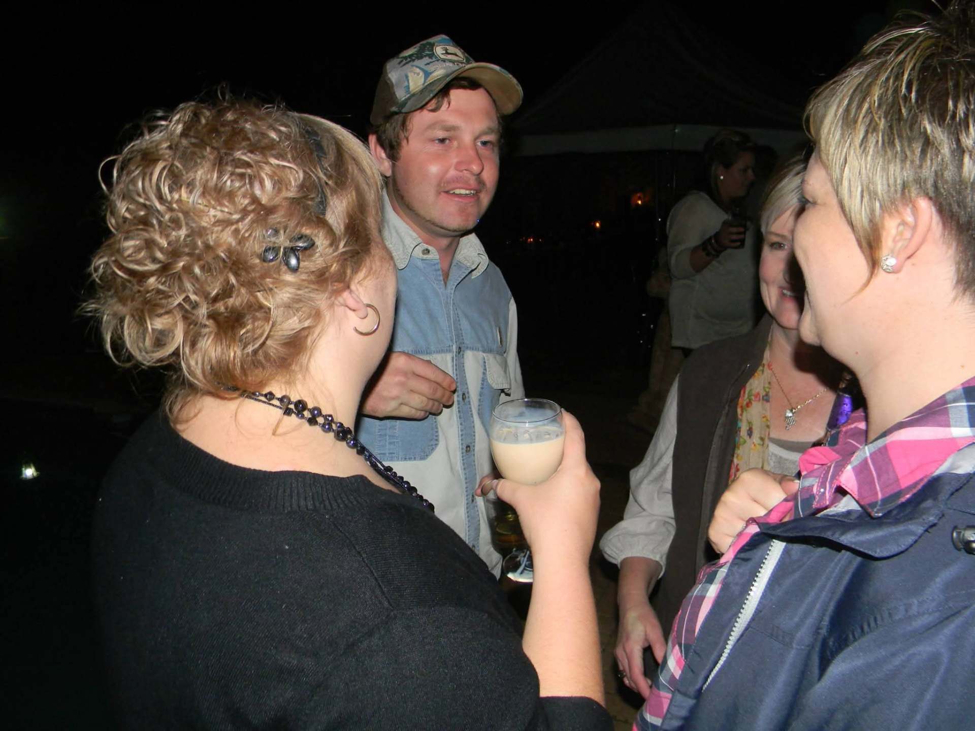 Angelo chatting with two smiling women over a glass at night