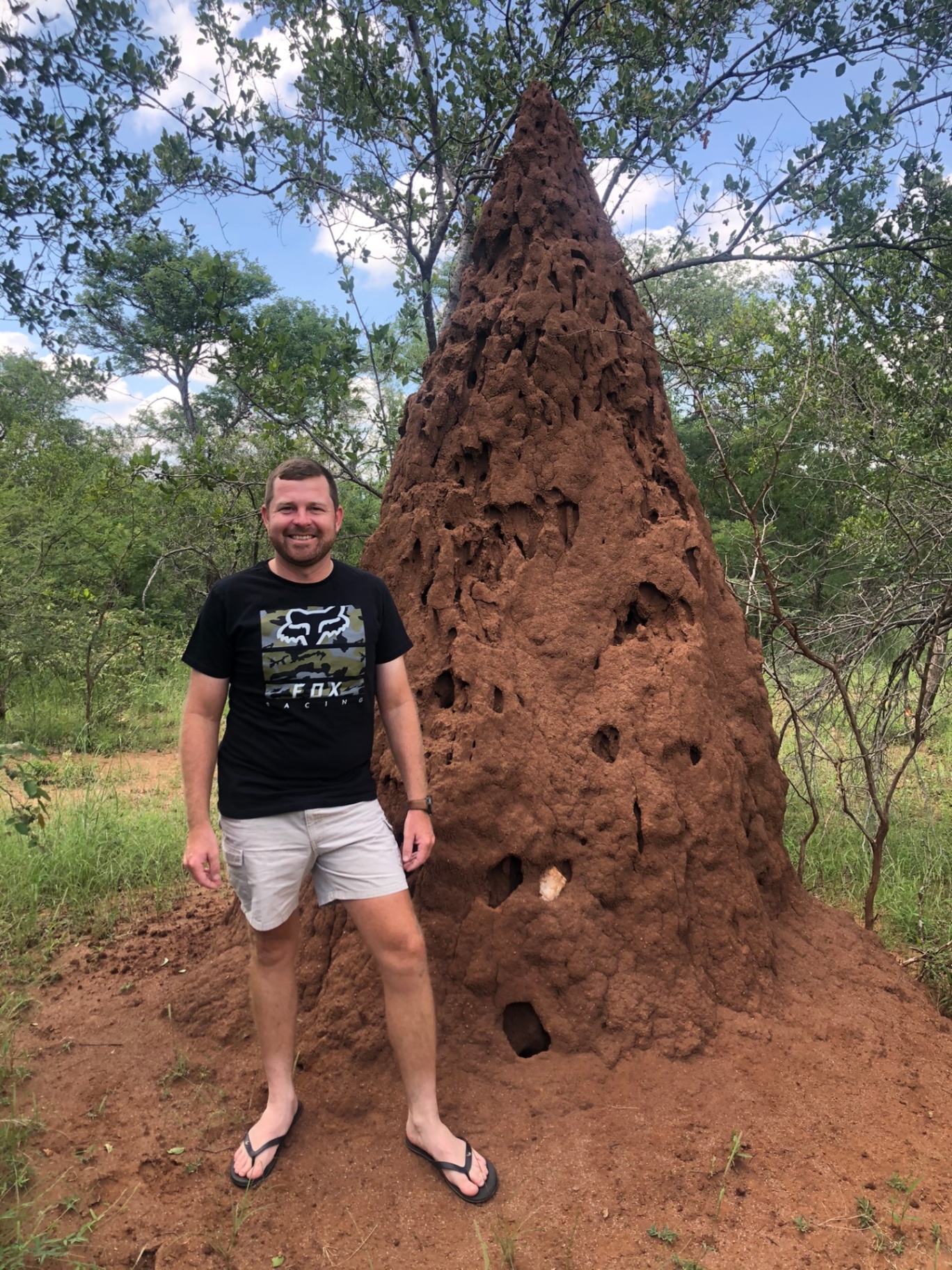 Angelo smiling beside a giant red termite mound in the bushveld