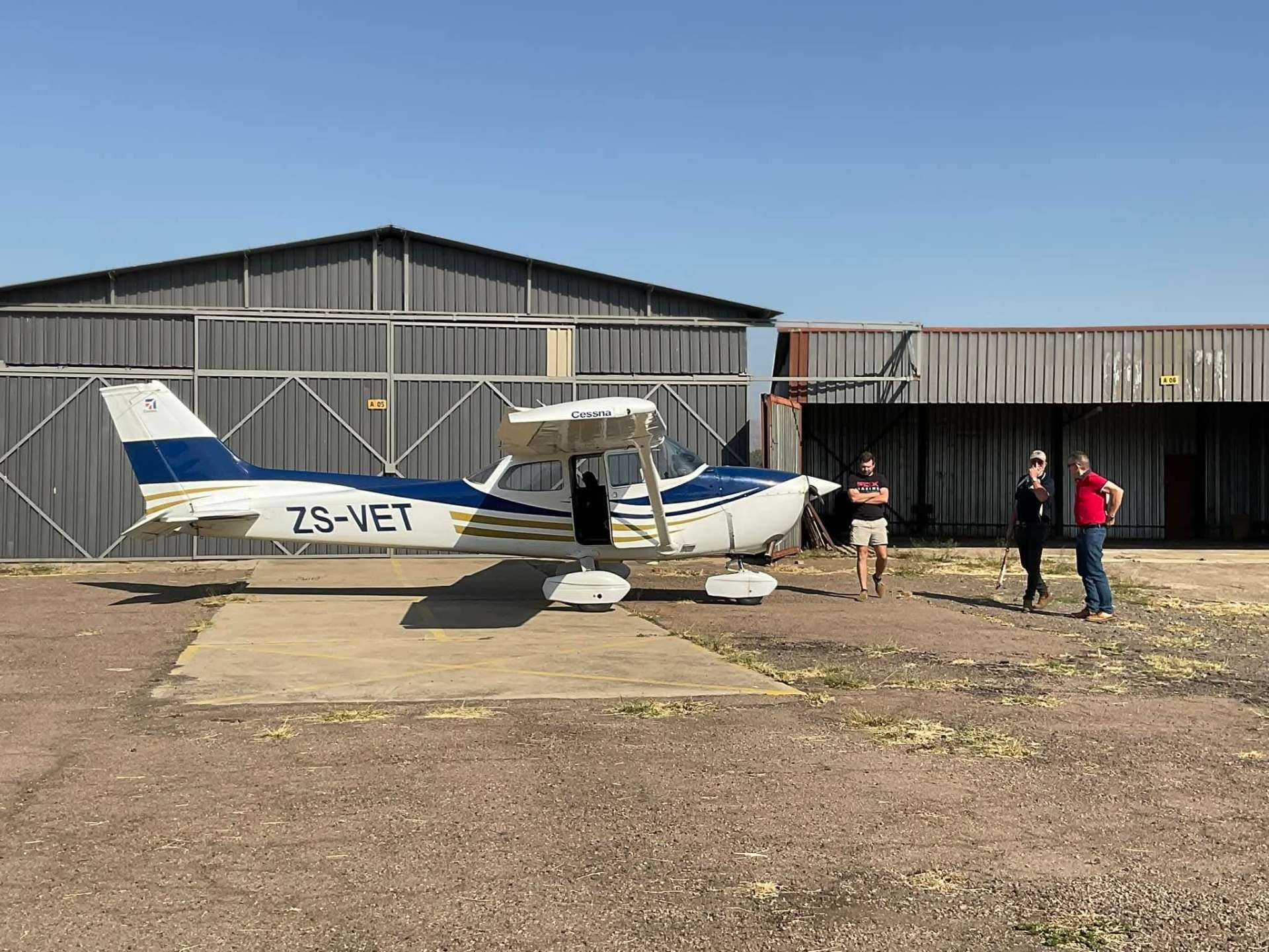 Angelo and two companions beside the white and blue Cessna ZS-VET outside the airfield hangars