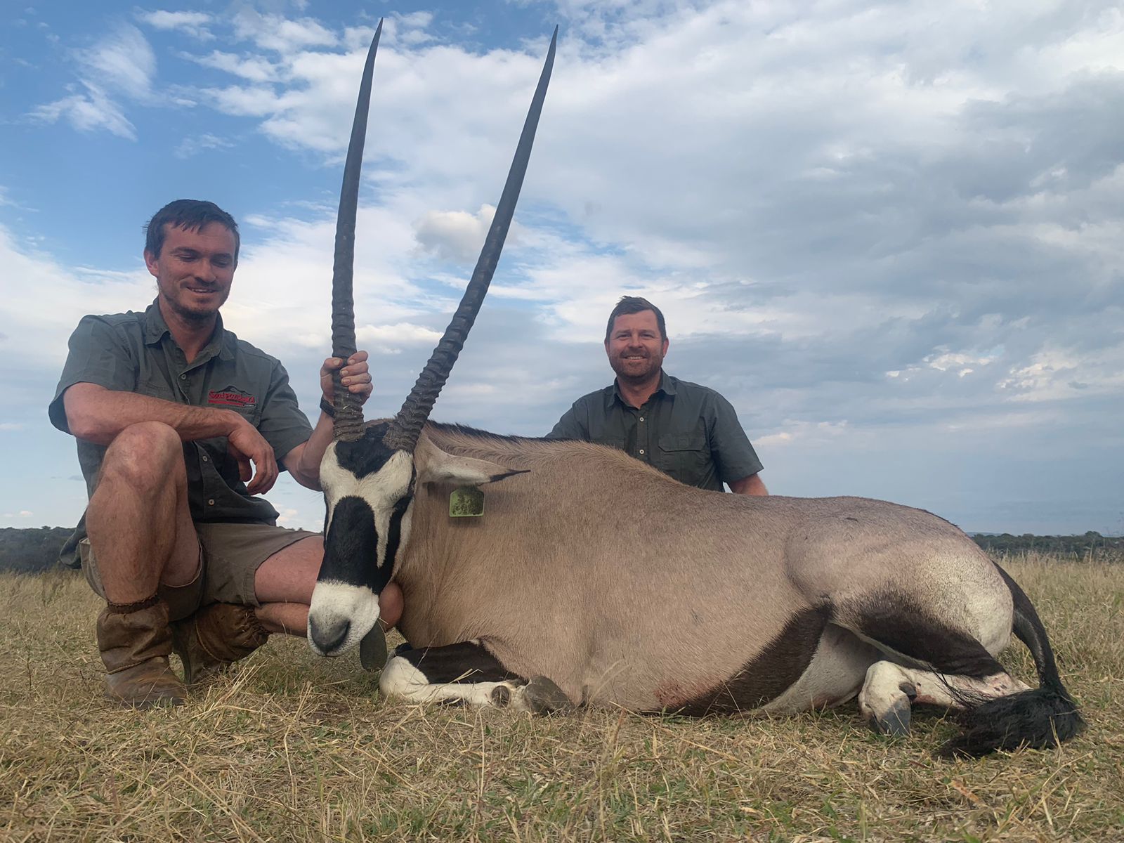 Angelo and Alwyn kneeling in the veld beside a gemsbok with long straight horns
