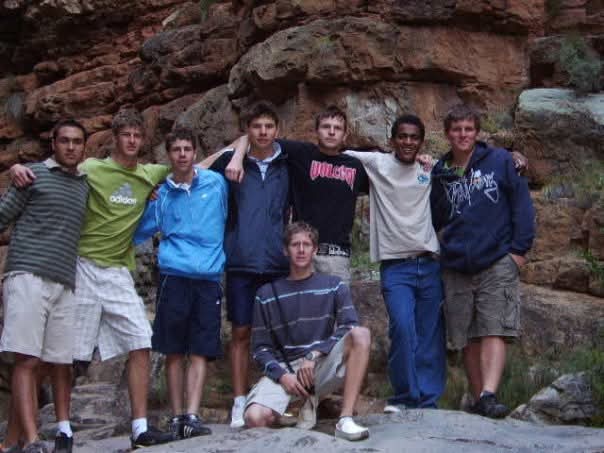A group of friends posing with arms around each other on a rocky cliff ledge