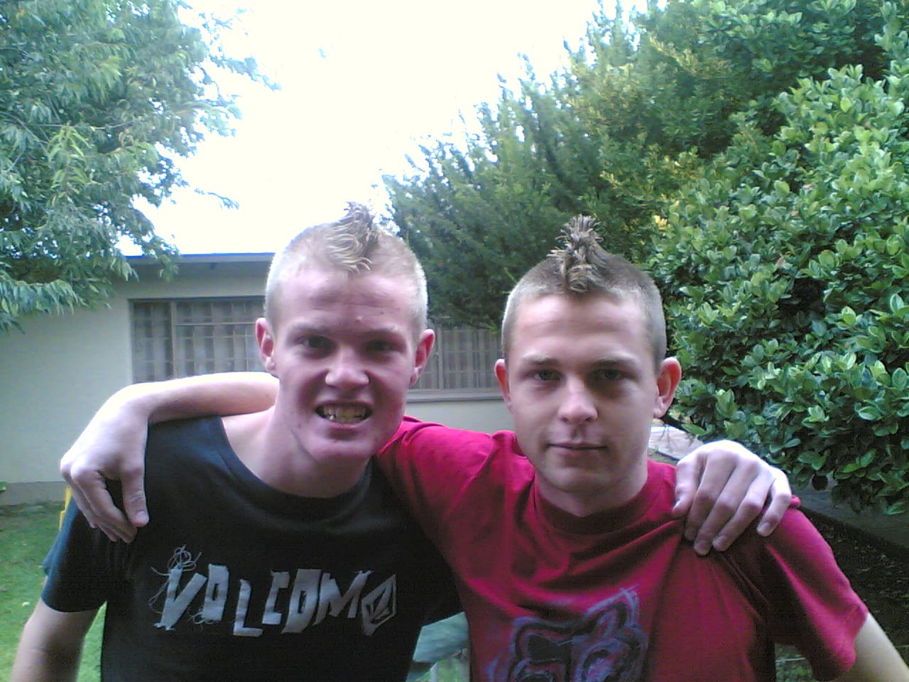 Angelo and his friend as teenagers with matching mohawks, arm around each other in the garden