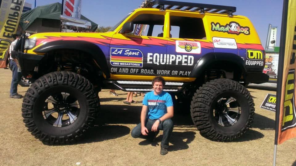 Angelo crouching beside a brightly coloured off-road truck with enormous tyres