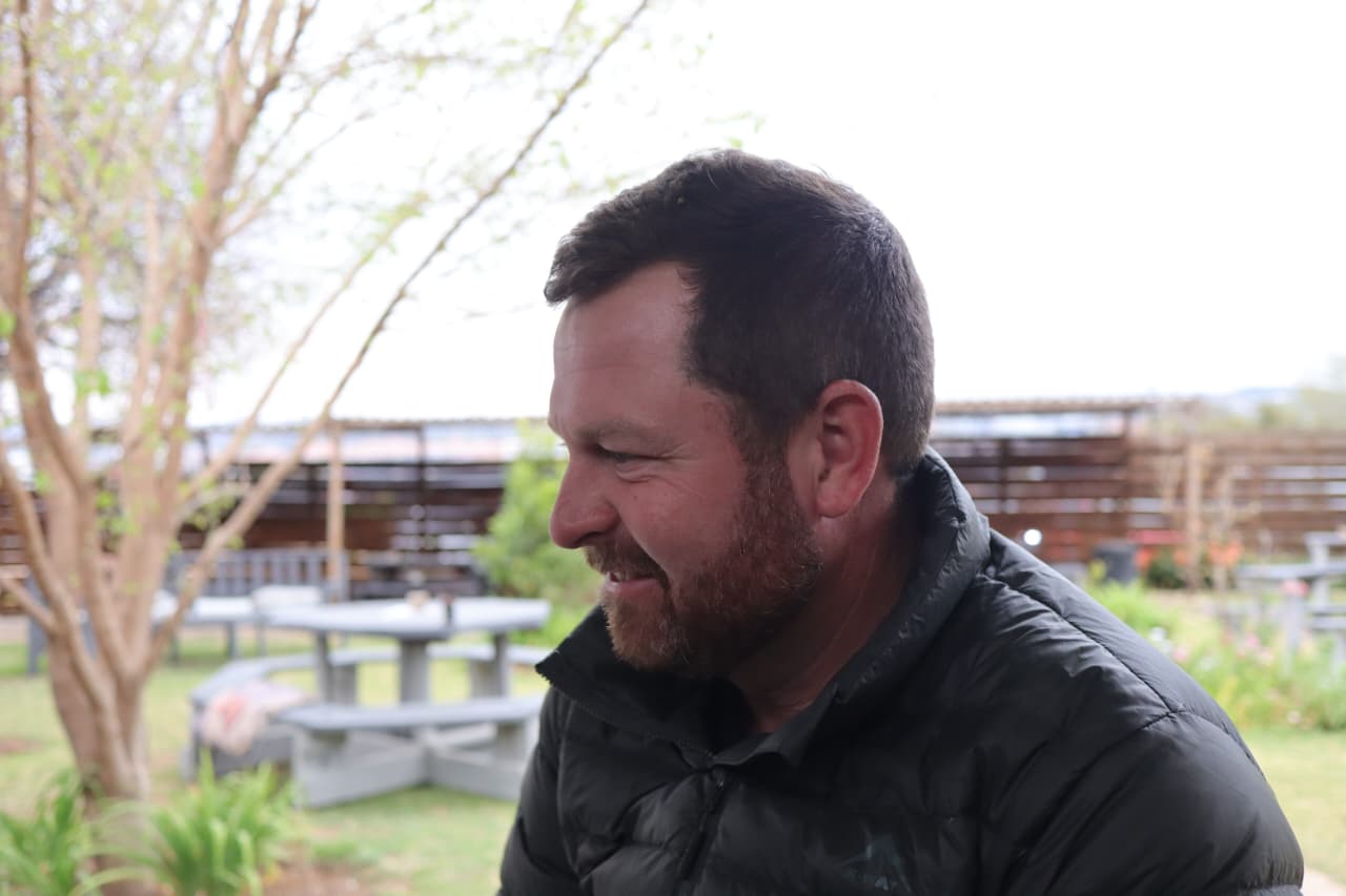Angelo in a black puffer jacket, smiling in side profile at a garden patio