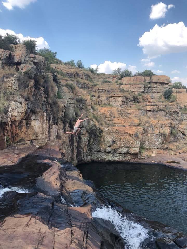 Angelo leaping from a rocky ledge with his arms stretched above the pool