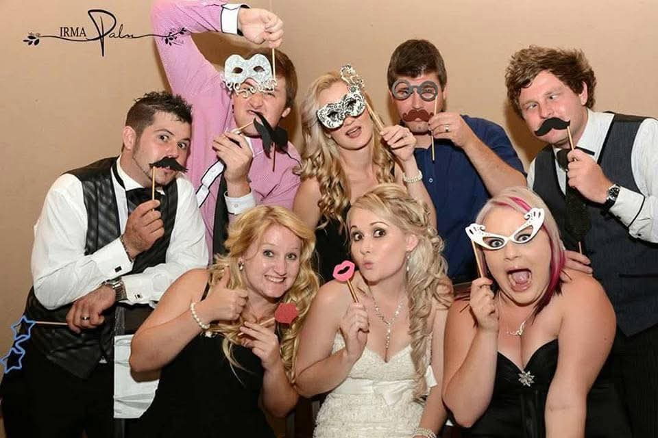Angelo and friends posing with party-prop masks and moustaches at a wedding