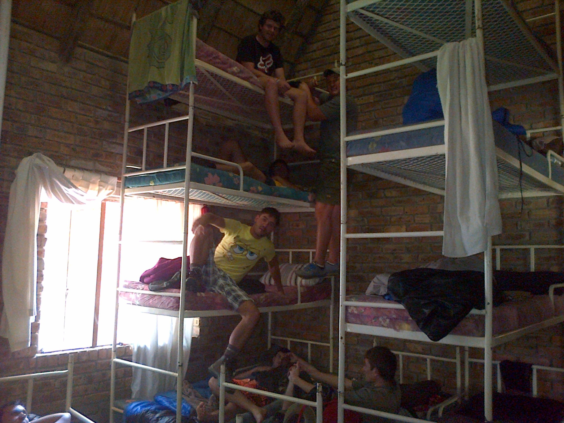 Friends joking around on stacked bunk beds in a brick hostel dormitory