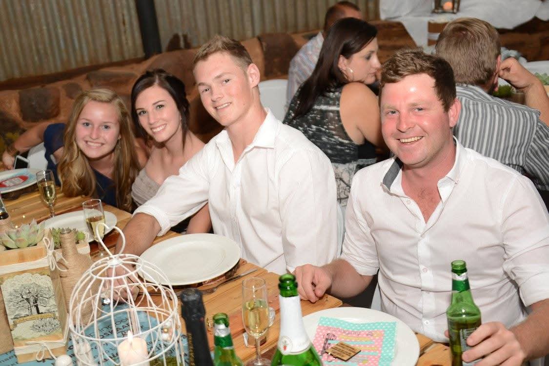 Four family members smiling together at a rustic dinner table
