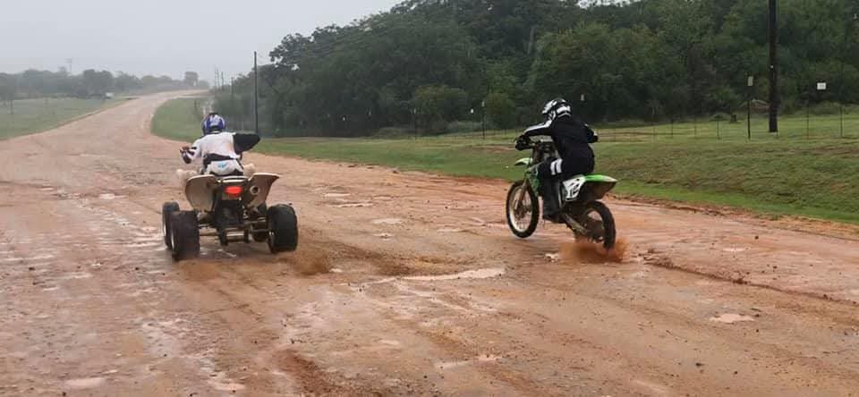 Angelo on his quad and a companion on a dirt bike riding away down the muddy track
