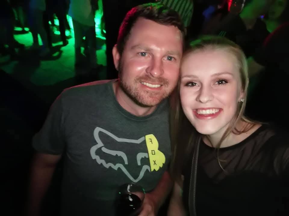 Angelo in a Fox Racing shirt taking a selfie with a smiling friend in a dim club