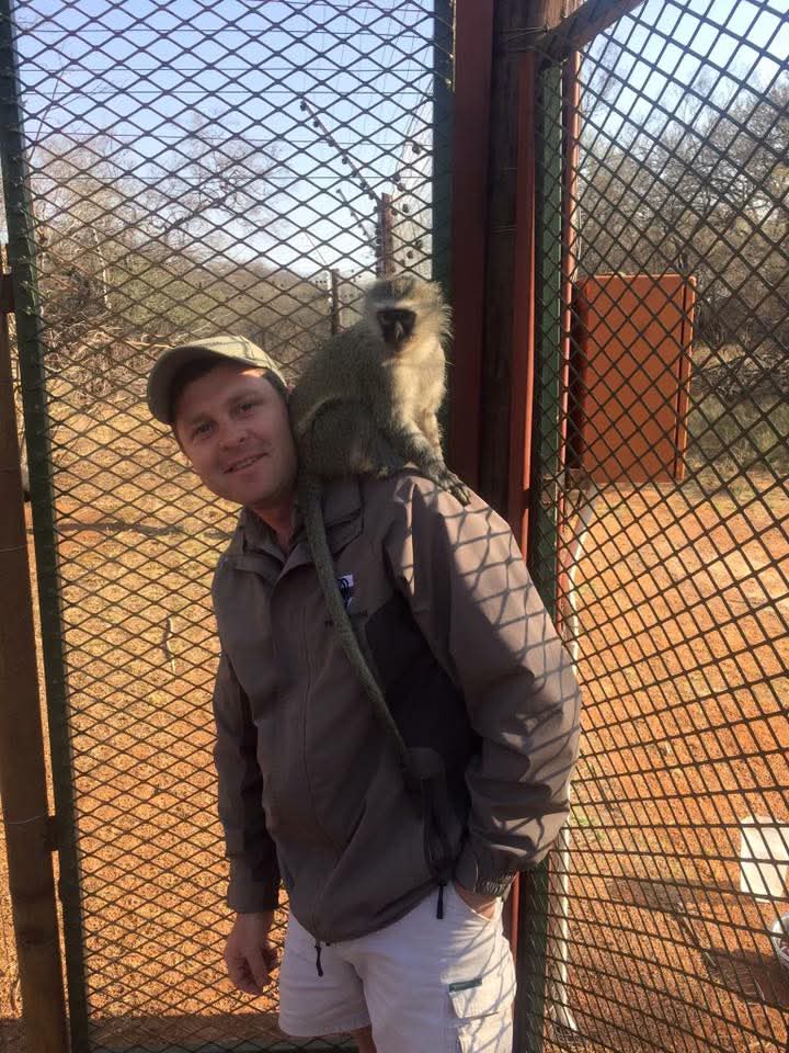 Angelo with a vervet monkey sitting on his shoulder beside a game fence