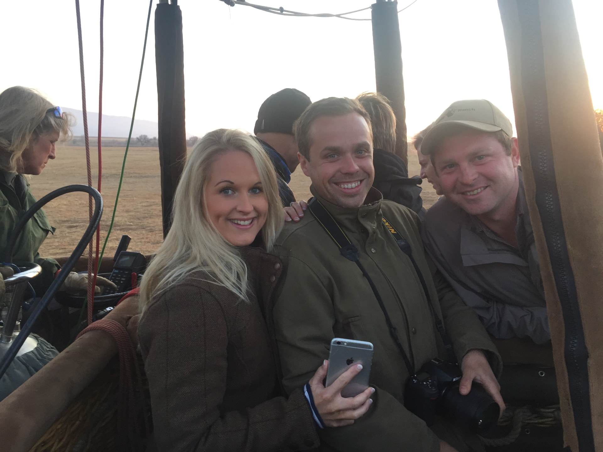 Friends smiling together in a hot-air balloon basket at sunrise over the open veld