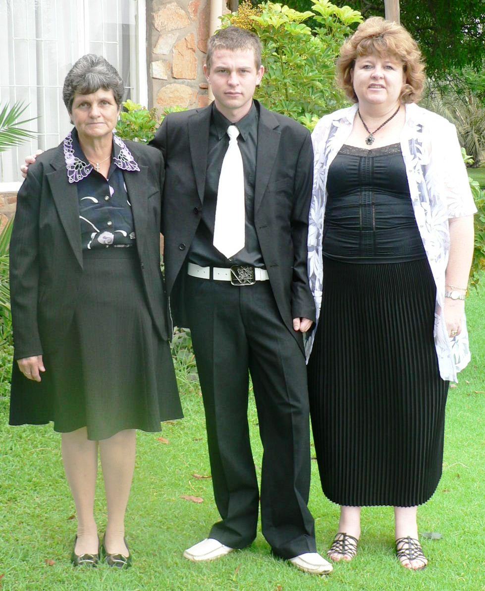 Angelo in a black suit and white tie between two family members on the lawn