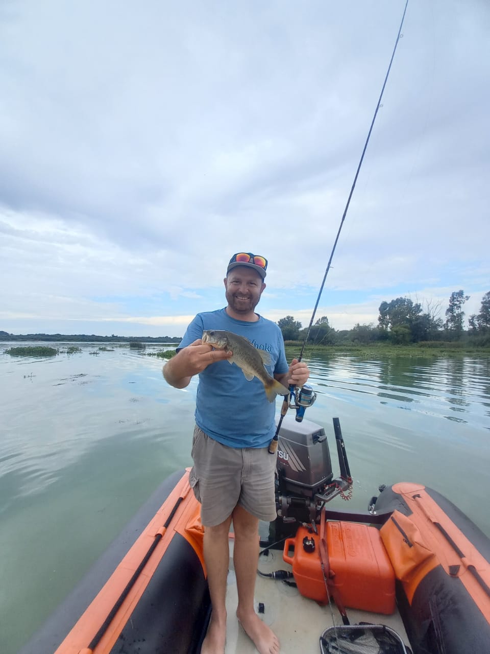 Angelo holding a bass on an inflatable boat under an overcast sky