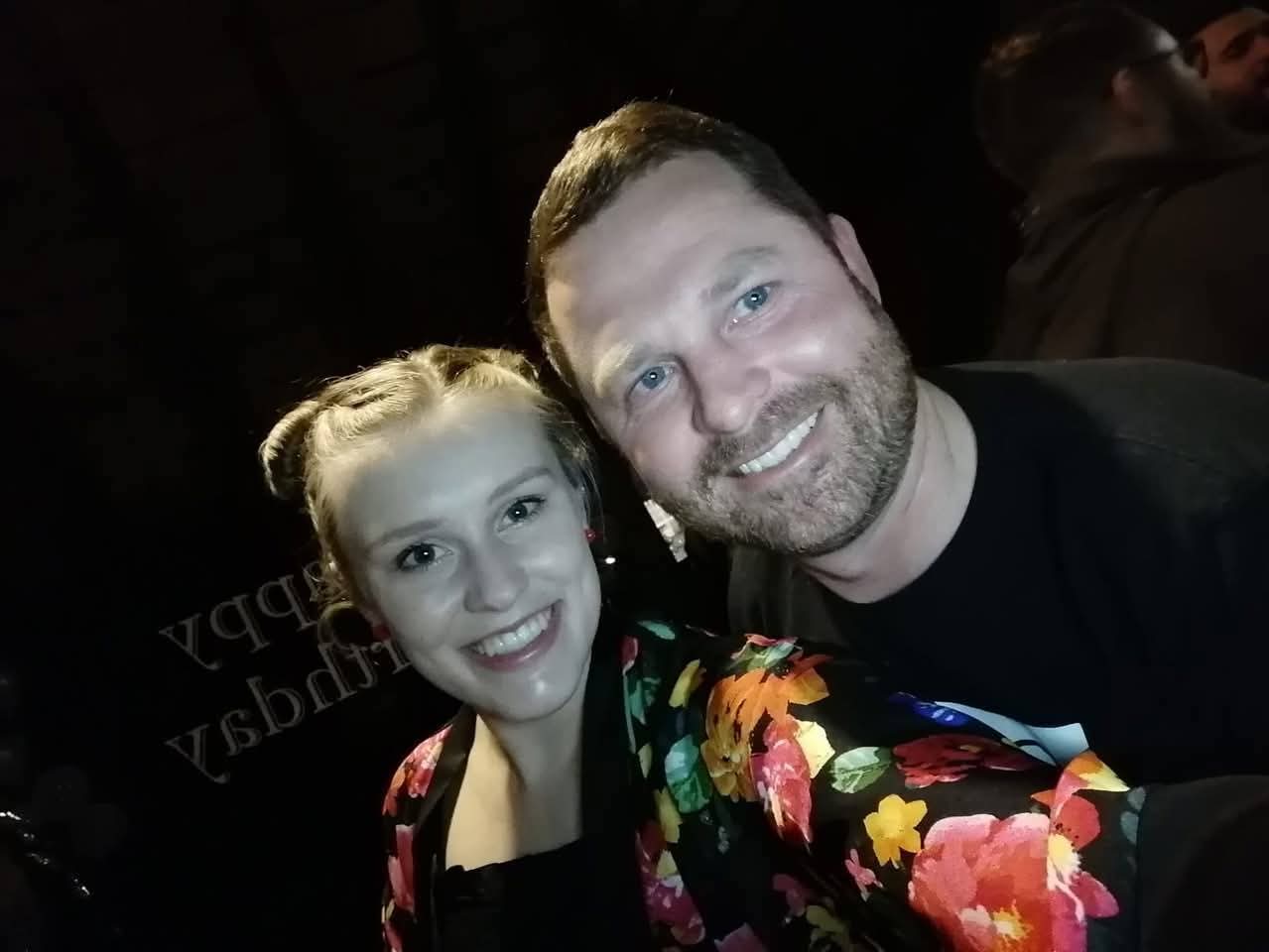 Angelo taking a selfie with a smiling friend in a floral jacket at a birthday party