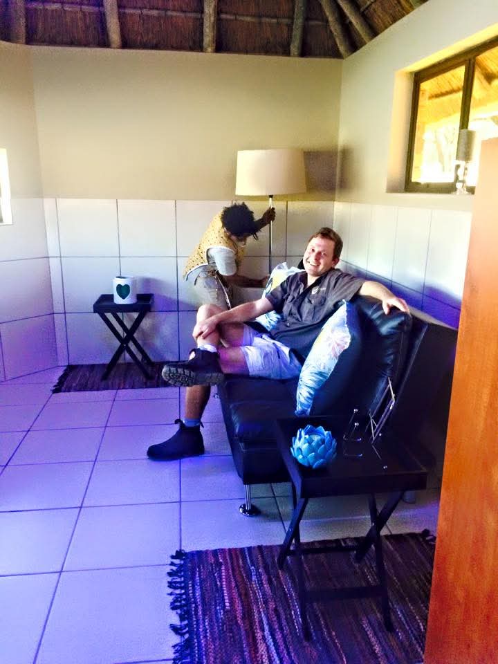 Angelo smiling on a black sofa inside a thatched room