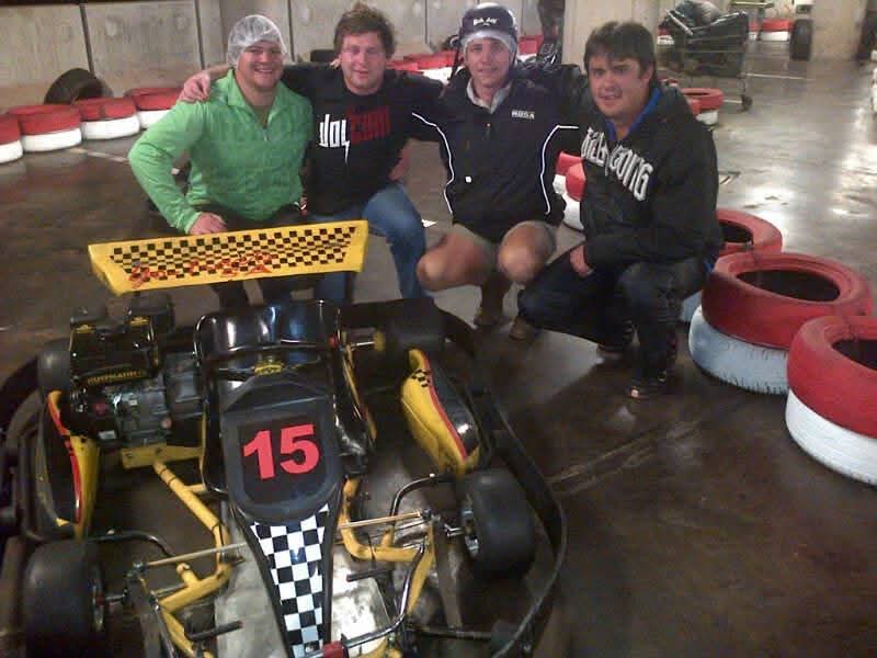 Four friends gathered beside kart number fifteen at an indoor track