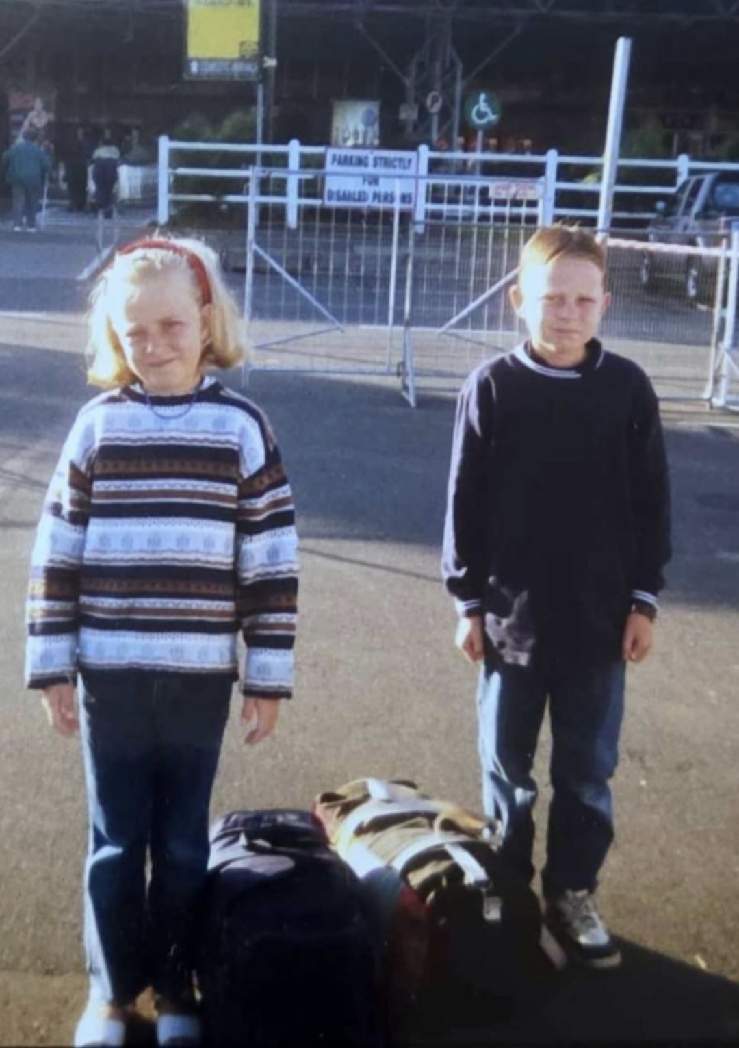 Angelo and his sister as children standing beside their luggage
