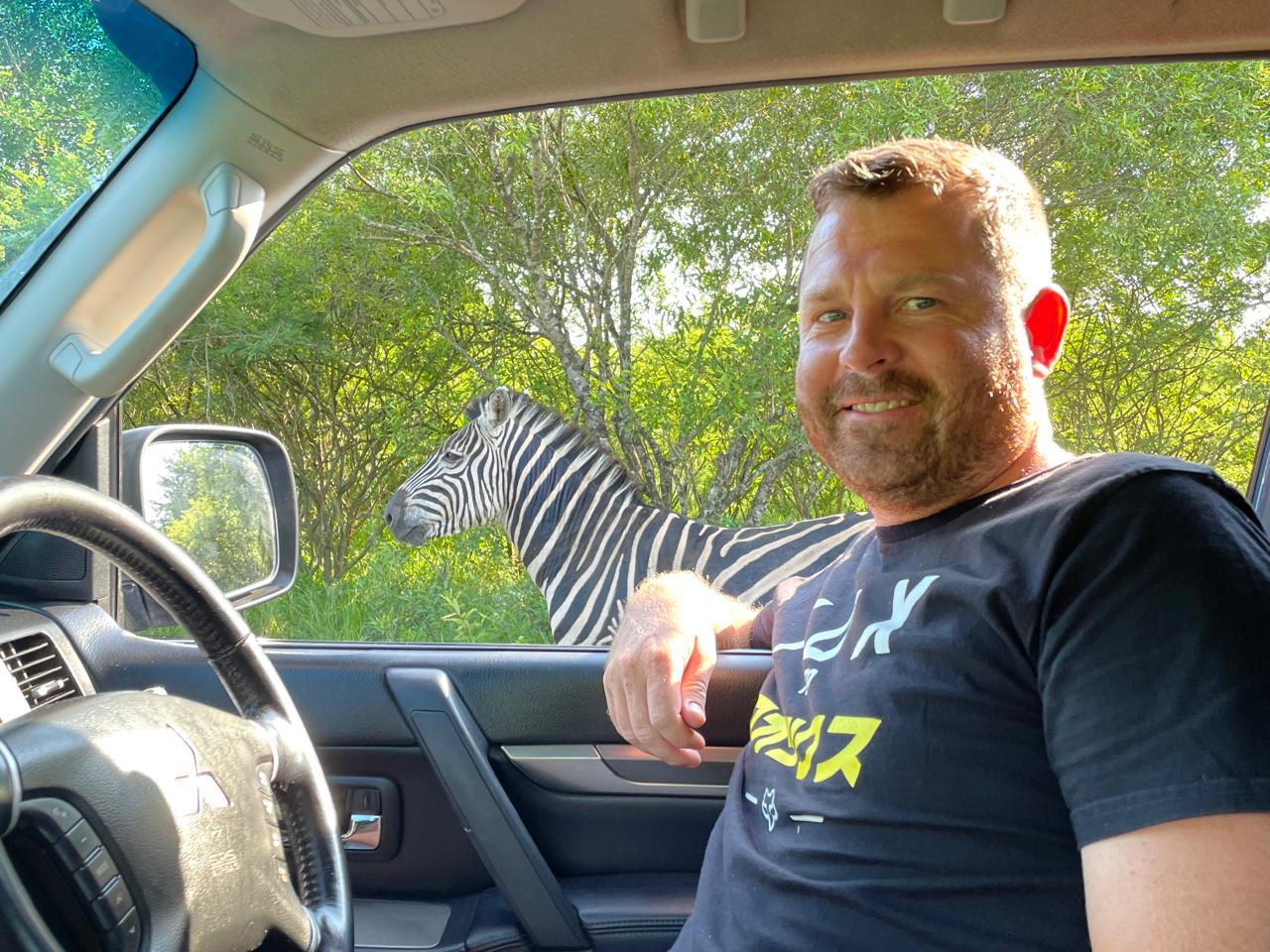 Angelo smiling behind the wheel of his truck with a zebra at the window