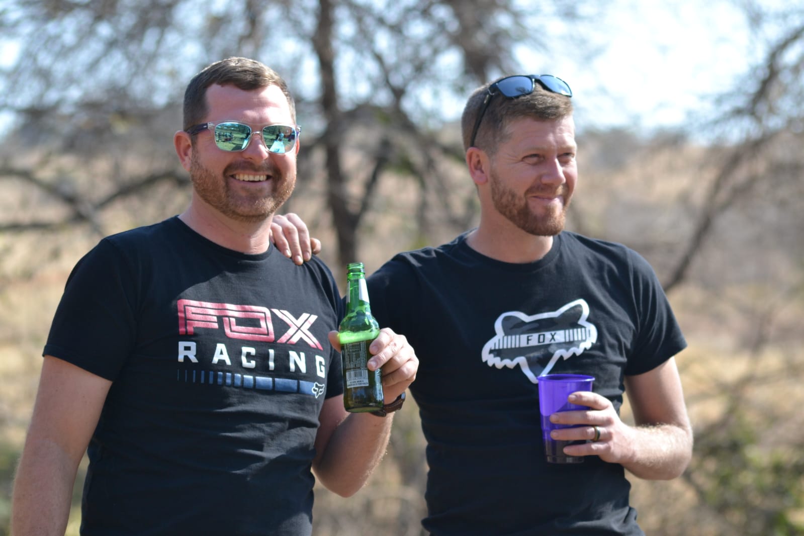 Angelo and a friend in Fox Racing shirts laughing with drinks in the bushveld
