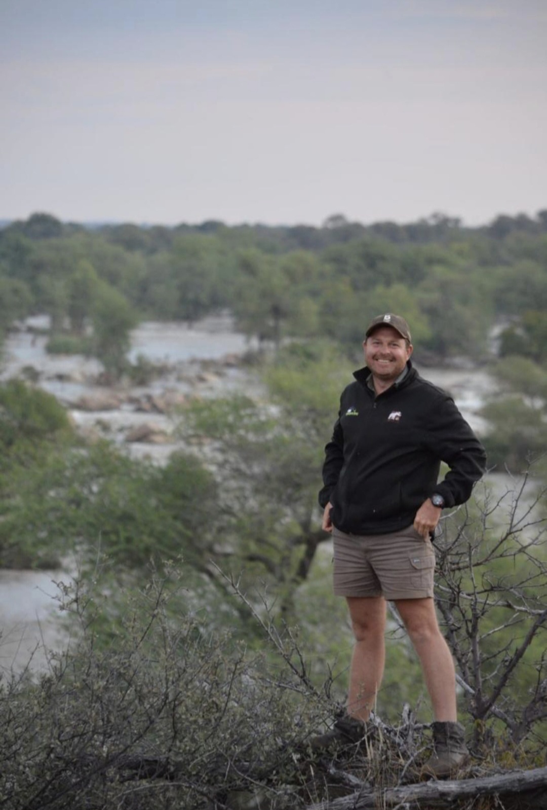 Angelo standing on a rocky hilltop overlooking a wide river and forest