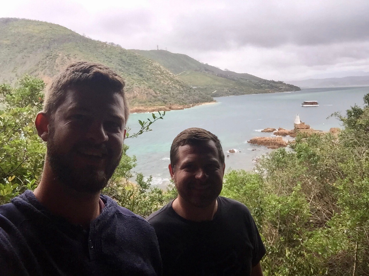 Angelo and his best friend taking a selfie above a bay with green hills behind them