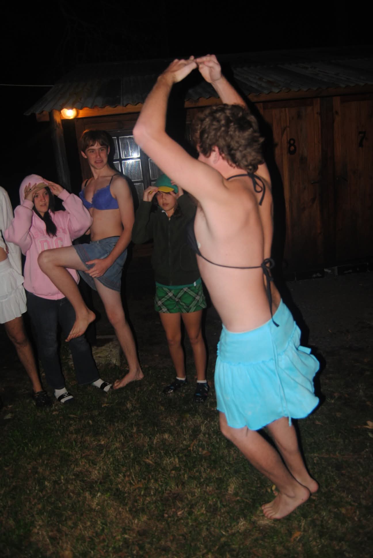 Angelo dancing in a blue skirt and bikini top at a night party