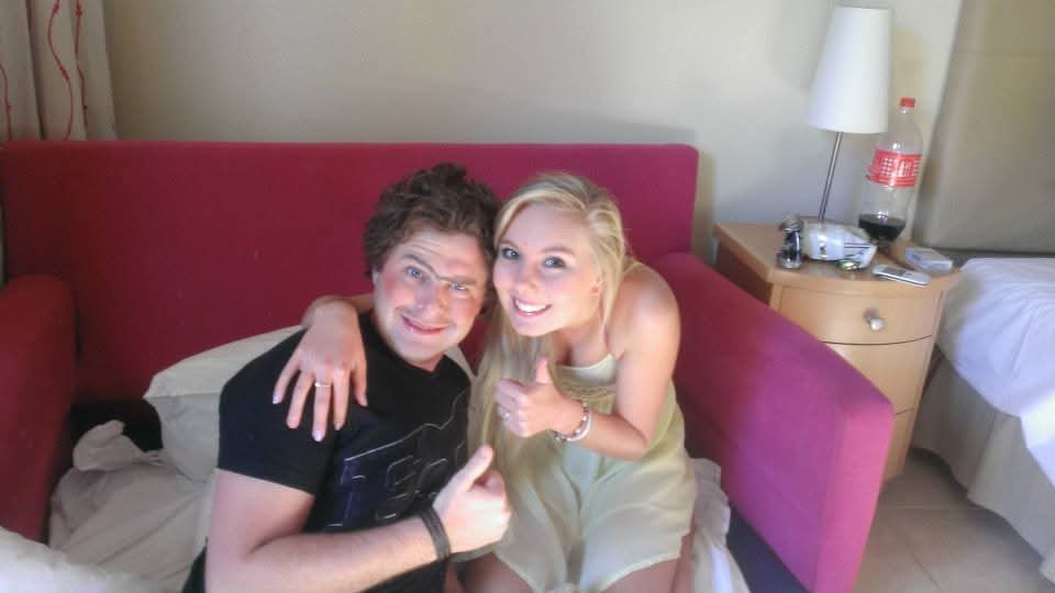 Angelo and a friend smiling and giving thumbs up on a red sofa