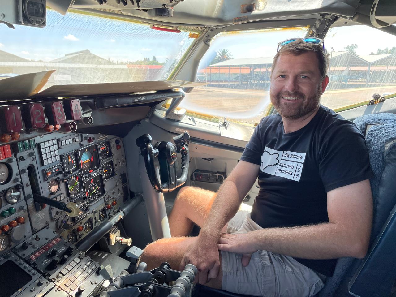 Angelo grinning in the pilot seat of a classic aircraft cockpit in full sunshine