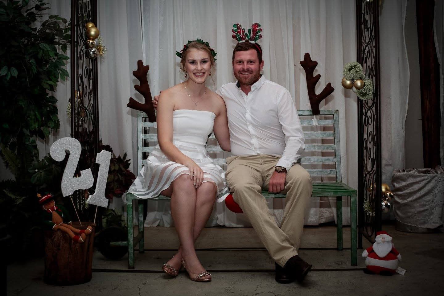 Angelo and a young woman in white sitting on a bench at a decorated 21st birthday photo corner